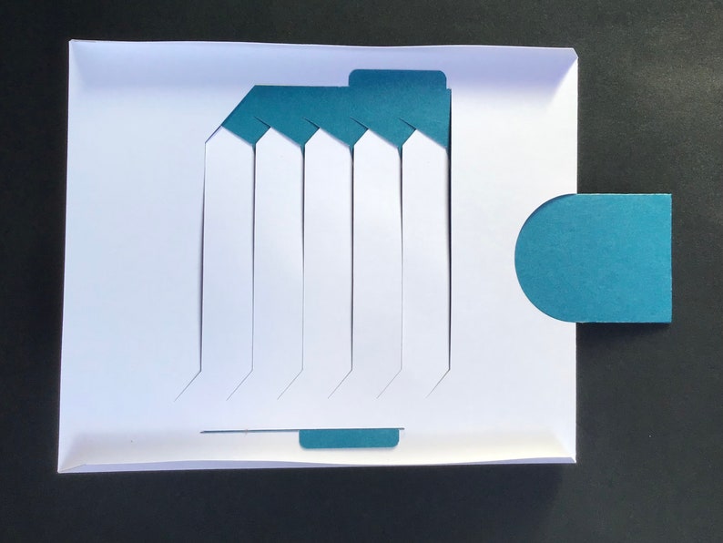 May include: A white card with a teal blue design. The card has seven vertical slots with a teal blue tab at the top and bottom. There is a teal blue semi-circle tab on the right side of the card.