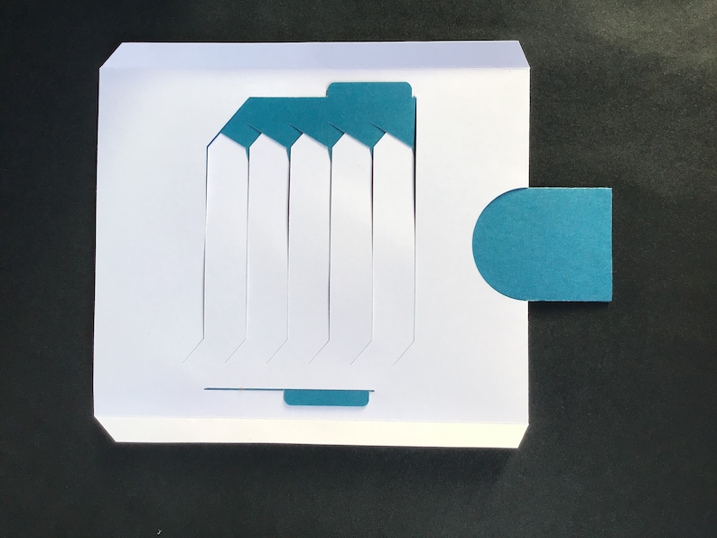 May include: A white card with a teal blue flap and a teal blue circle. The card has seven vertical slots cut out of it.