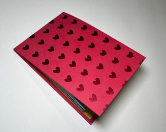 May include: A red card with a pattern of small, dark red hearts. The card is folded in half and the edges are visible.