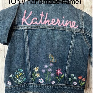 May include: A denim jacket with embroidered flowers and a butterfly design. The name "Katherine" is embroidered in pink thread across the back. The jacket features a classic collar, button closures, and pockets.