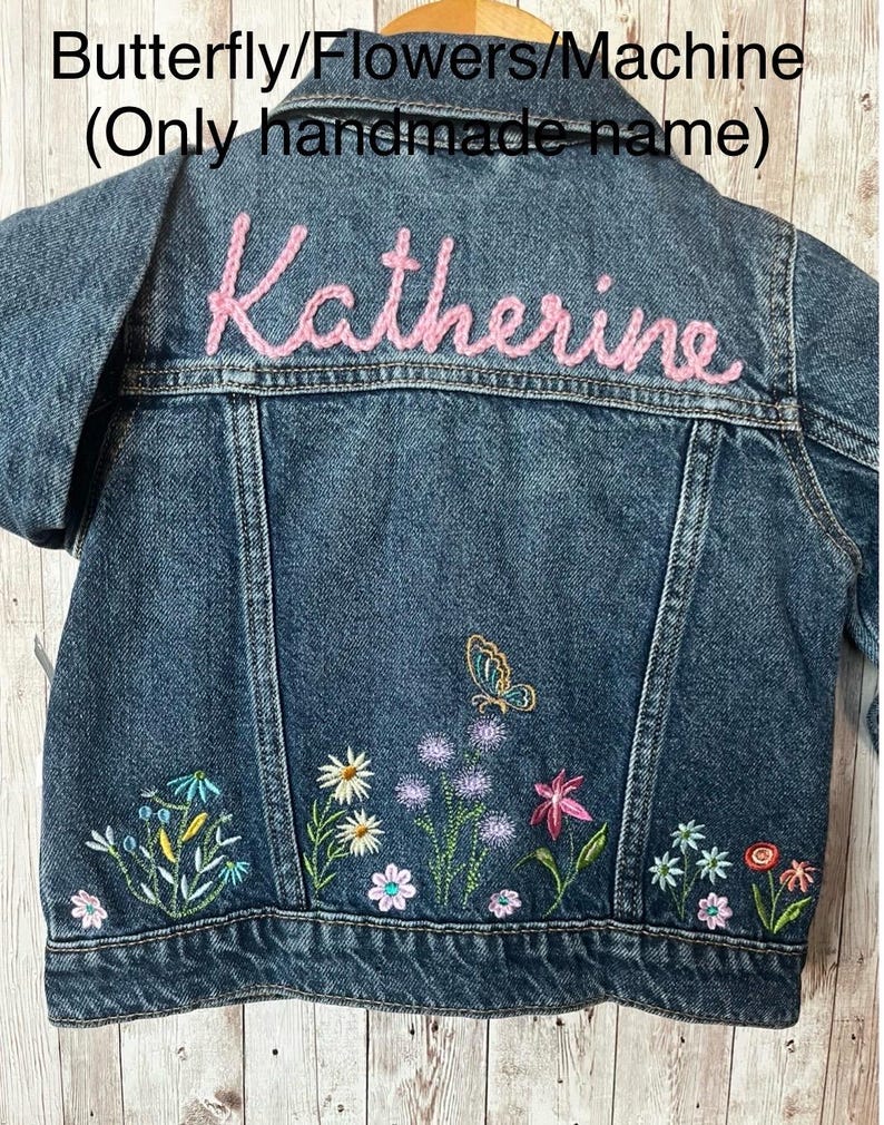 May include: A denim jacket with embroidered flowers and a butterfly design. The name "Katherine" is embroidered in pink thread across the back. The jacket features a classic collar, button closures, and pockets.