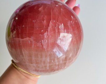 Könnte beinhalten: Eine große, polierte Kristallkugel in Rosa und Weiß. Die Kugel ist glatt und hat eine durchscheinende Optik.