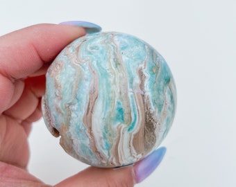 May include: A blue, green, and brown agate sphere with swirling patterns. The sphere is smooth and polished.