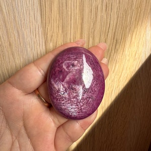 May include: A smooth, oval-shaped pink and white gemstone with a swirling pattern. The gemstone is polished and has a glossy finish.