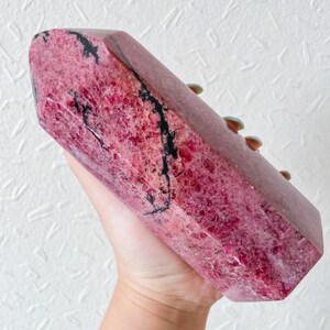 May include: A large, pink and black, polished,  faceted,  crystal point. The crystal has a natural, rough texture.