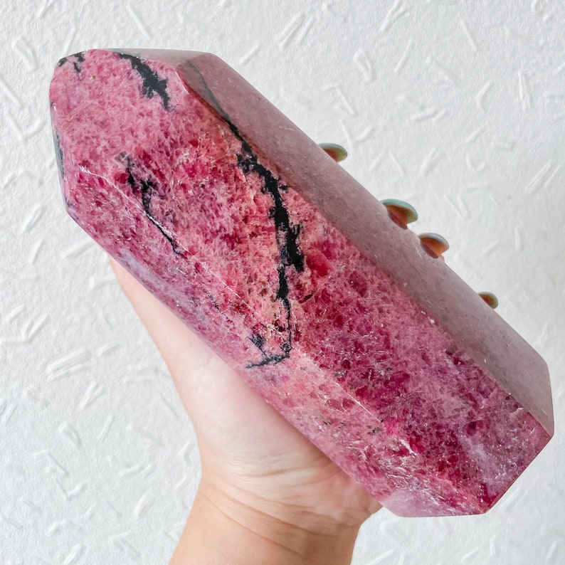 May include: A large, pink and black, polished,  faceted,  crystal point. The crystal has a natural, rough texture.