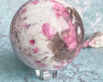 May include: A pink and white crystal sphere with a clear stand. The sphere has a swirling pattern of pink and white.