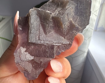 May include: A large, dark purple fluorite crystal with a geometric, faceted structure. The crystal has a rough, textured surface and is a natural, raw specimen.