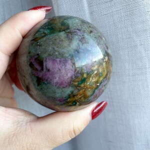 May include: A green, brown and purple sphere with a swirling pattern. The sphere is made of polished stone.