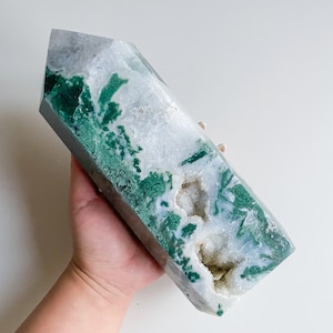 May include: A large green and white agate crystal point with a natural druzy formation. The crystal is polished and has a smooth, glassy surface.