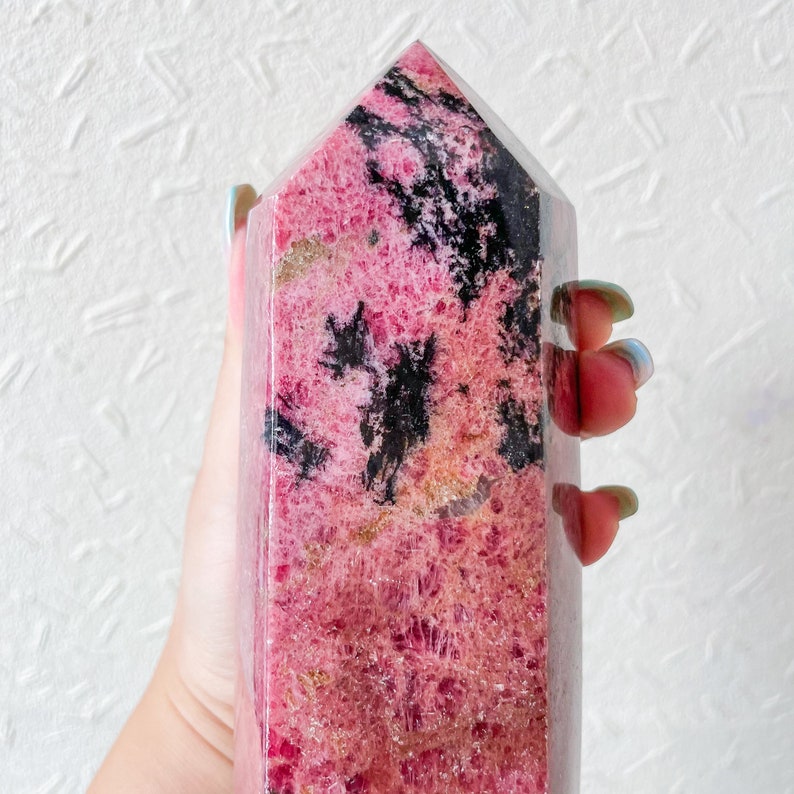 May include: A pink and black crystal point, also known as a raw crystal, with a pointed top and a flat base. The crystal has a natural, rough texture and is a popular choice for crystal healing and meditation.