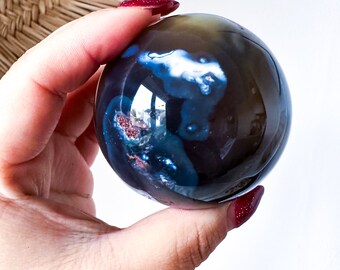 May include: A polished blue agate sphere with brown and white inclusions. The sphere is smooth and has a high gloss finish.
