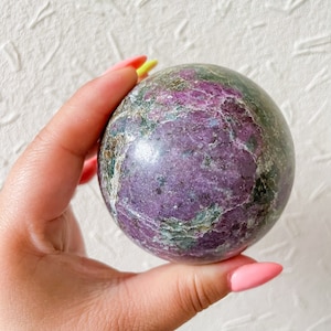 May include: A purple and green sphere made of polished stone. The sphere has a swirling pattern of purple, green, and white.