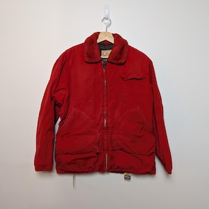 May include: A red corduroy jacket with a faux fur collar, a zipper closure, and multiple pockets. The jacket is hanging on a wooden hanger against a white wall. The jacket has a vintage look.