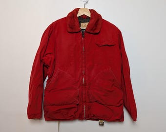 May include: A red corduroy jacket with a faux fur collar, a zipper closure, and multiple pockets. The jacket is hanging on a wooden hanger against a white wall. The jacket has a vintage look.