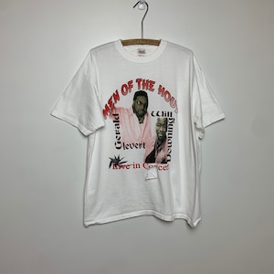 May include: White t-shirt with a graphic print of two men. The text reads "Men of the House" with the names "Gerald Levert" and "Will Downing" printed below the image. The text "Live in Concert" is printed below the names.