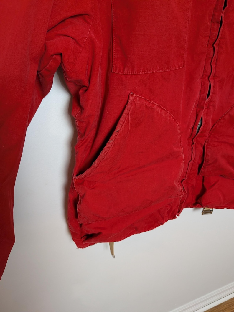 May include: Close-up of a red jacket with a pocket and a zipper. The jacket is made of a soft material and has a worn appearance. The jacket's colour is a vibrant red.