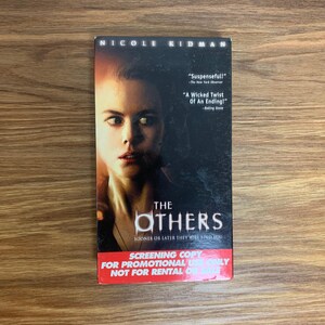 Op de afbeelding: Een DVD-hoes met Nicole Kidman op de voorkant. De titel van de film is "The Others" en de tagline is "Sooner or later they will find you". De hoes is gemarkeerd als een screeningskopie voor promotioneel gebruik en is niet bedoeld voor verhuur.