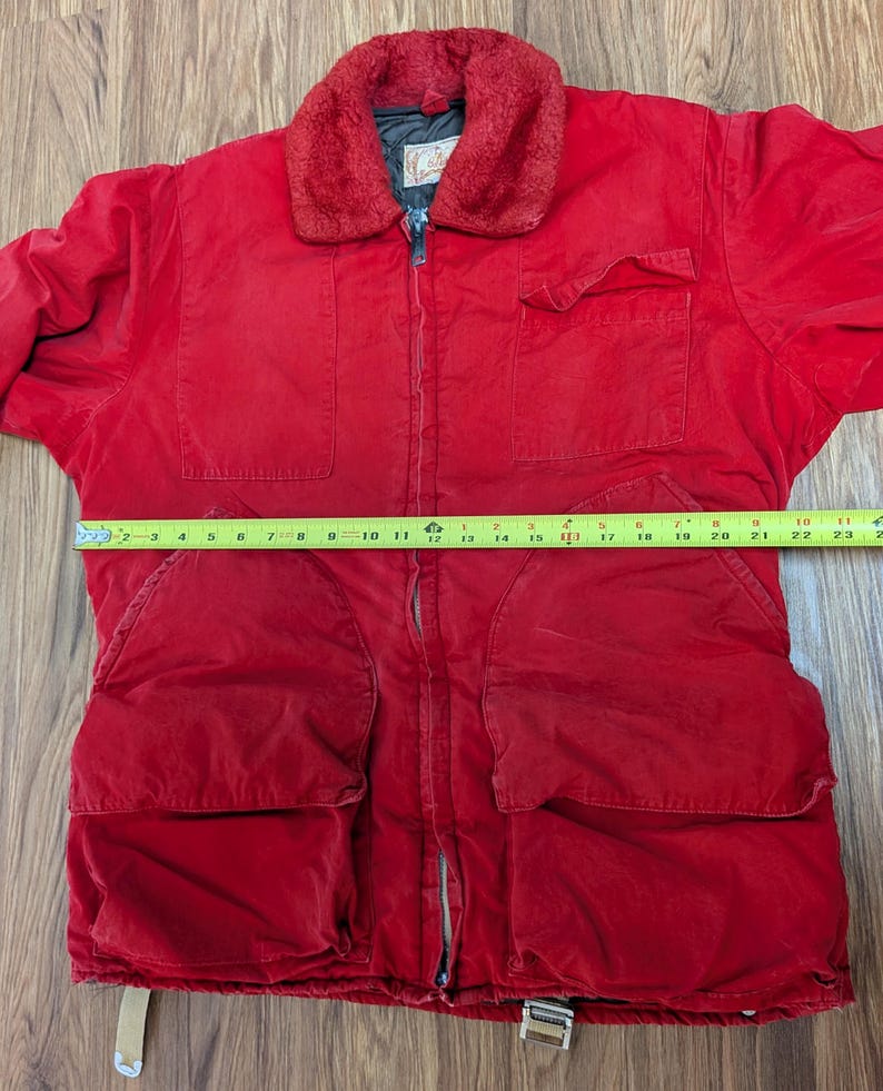 May include: A red corduroy jacket with a faux fur collar. The jacket has a zipper closure, multiple pockets, and a tan strap at the bottom. The jacket is approximately 58 cm long.