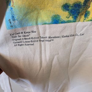 May include: A cream-colored sweatshirt featuring a vibrant yellow, blue, and green graphic print. Text reads: Kid Cudi & Kanye West "Kids See Ghosts" Original Artwork &copy;2018 Takashi Murakami / Kaikai Kiki Co., Ltd. Garment Layout &copy;2018 Virgil Abloh&trade;.