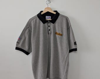 May include: A grey and black short-sleeve polo shirt featuring the Steelers logo embroidered on the chest. The shirt has a black collar, a three-button placket, and Pro Line and Starter branding on the sleeves. The label reads Pro Line.