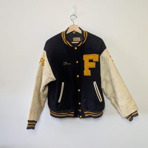 Può includere: Una giacca varsity nera con maniche color bianco sporco, caratterizzata da una grande lettera F gialla sul petto sinistro e dal nome Tony ricamato in corsivo giallo a destra. Presenta polsini, colletto e orlo a coste a righe gialle e nere con bottoni.