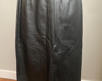 May include: A black leather skirt with a straight cut. The skirt features a high waist and a knee-length hem. Vertical seams are visible on the front and back, providing a tailored appearance. The skirt is crafted from smooth, glossy leather.