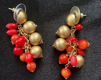 May include: Gold tone dangle earrings with red and orange beads. The earrings have a chain link design and are accented with small gold balls.