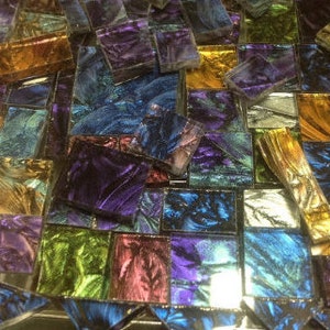 May include: Assortment of iridescent glass mosaic tiles in shades of blue, green, purple, and gold. The tiles are arranged in a random pattern and have a textured surface.