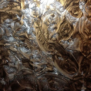 May include: Close-up of a textured surface with a swirling pattern in shades of gold and silver.