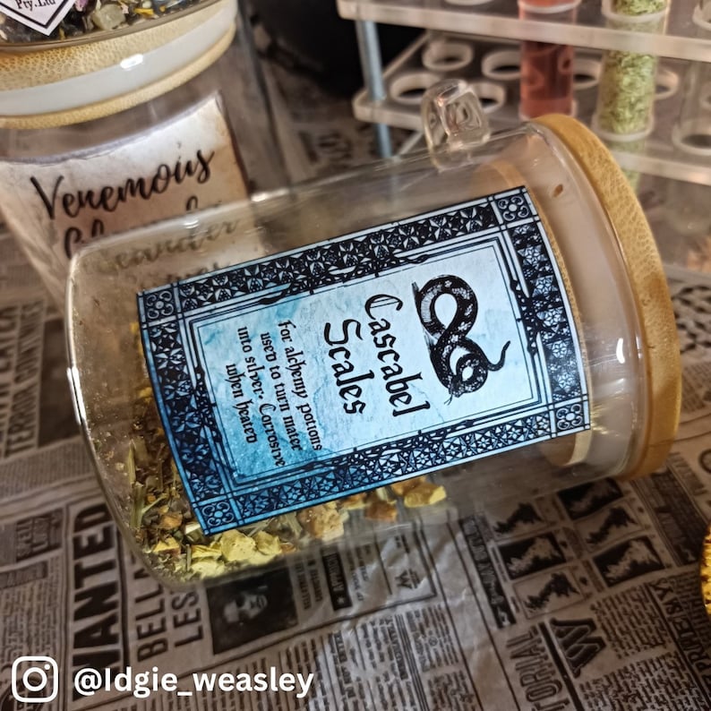 May include: A glass jar with a wooden lid filled with dried herbs and a label that reads "Cascabel Scales. For alchemy potions used to turn matter into silver. Corrosive when heated."