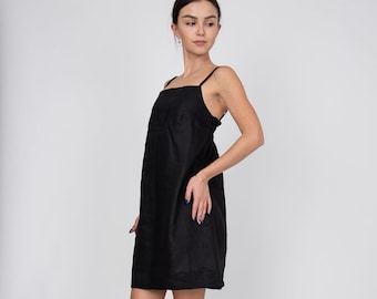May include: A woman wearing a black sleeveless dress and nude heeled sandals. The dress has a square neckline and a straight silhouette.