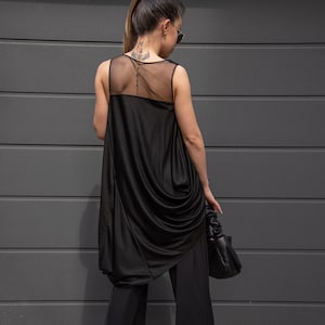 K&ouml;nnte beinhalten: Ein schwarzes &auml;rmelloses Oberteil mit einem durchsichtigen Mesh-R&uuml;ckenpanel und einem drapierten Design. Das Oberteil wird mit einer schwarzen weiten Hose kombiniert.