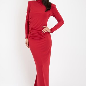 May include: A long-sleeved, red maxi dress with a high neck and a fitted silhouette. The dress has a slight ruffle detail at the shoulders and a gathered skirt.