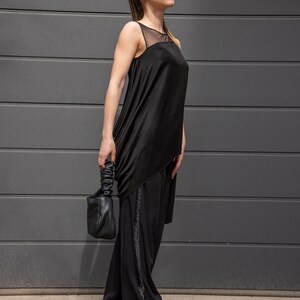 K&ouml;nnte beinhalten: Eine Frau tr&auml;gt ein schwarzes asymmetrisches Oberteil mit einem durchsichtigen Einsatz und eine schwarze weite Hose mit einem Satinband an der Seite. Sie tr&auml;gt eine schwarze Lederhandtasche und eine Sonnenbrille.