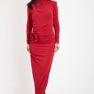 May include: A long, red dress with a high neck and long sleeves. The dress has a large, red flower detail on the side.