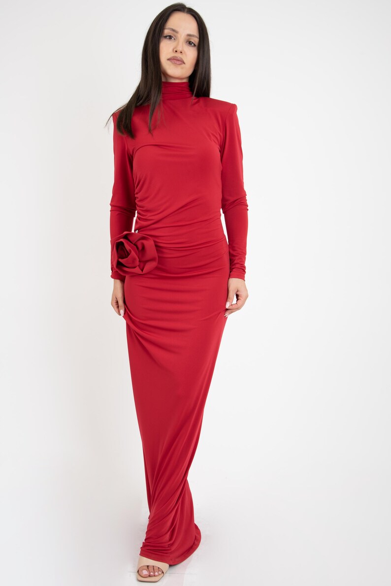 May include: A long, red dress with a high neck and long sleeves. The dress has a large, red flower detail on the side.