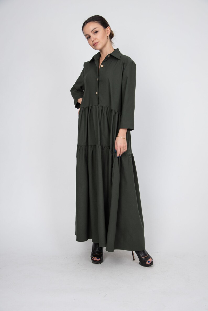 May include: A long-sleeved, dark green, button-down dress with a tiered skirt. The dress has a collared neckline and a relaxed fit.