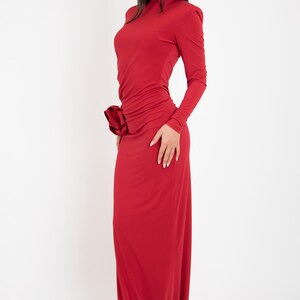May include: A long, red, form-fitting dress with a high neck and long sleeves. The dress has a gathered detail at the waist.
