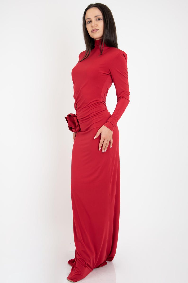 May include: A long, red, form-fitting dress with a high neck and long sleeves. The dress has a gathered detail at the waist.