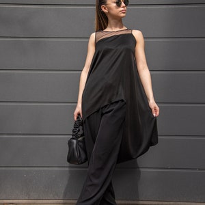 K&ouml;nnte beinhalten: Eine Frau tr&auml;gt ein schwarzes &auml;rmelloses Oberteil mit einem durchsichtigen &Uuml;berwurf und eine schwarze weite Hose. Sie h&auml;lt eine schwarze Handtasche und tr&auml;gt eine Sonnenbrille.
