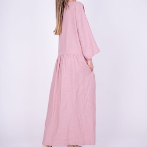 May include: A long, loose-fitting, pink linen dress with 3/4 sleeves and pockets. The dress is made of a soft, comfortable fabric and has a relaxed fit.