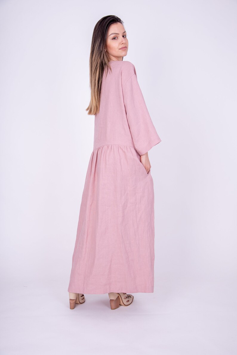 May include: A long, loose-fitting, pink linen dress with 3/4 sleeves and pockets. The dress is made of a soft, comfortable fabric and has a relaxed fit.