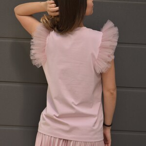 May include: A pink t-shirt with tulle ruffle sleeves and a matching pink pleated skirt.