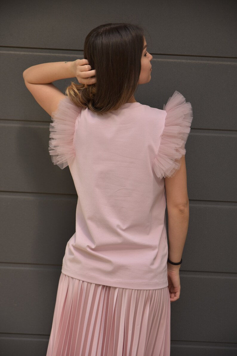 May include: A pink t-shirt with tulle ruffle sleeves and a matching pink pleated skirt.