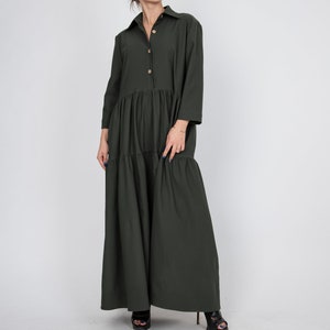 May include: A long, dark green, tiered dress with a button-up collar and long sleeves. The dress has a relaxed fit and is made of a soft, comfortable fabric.