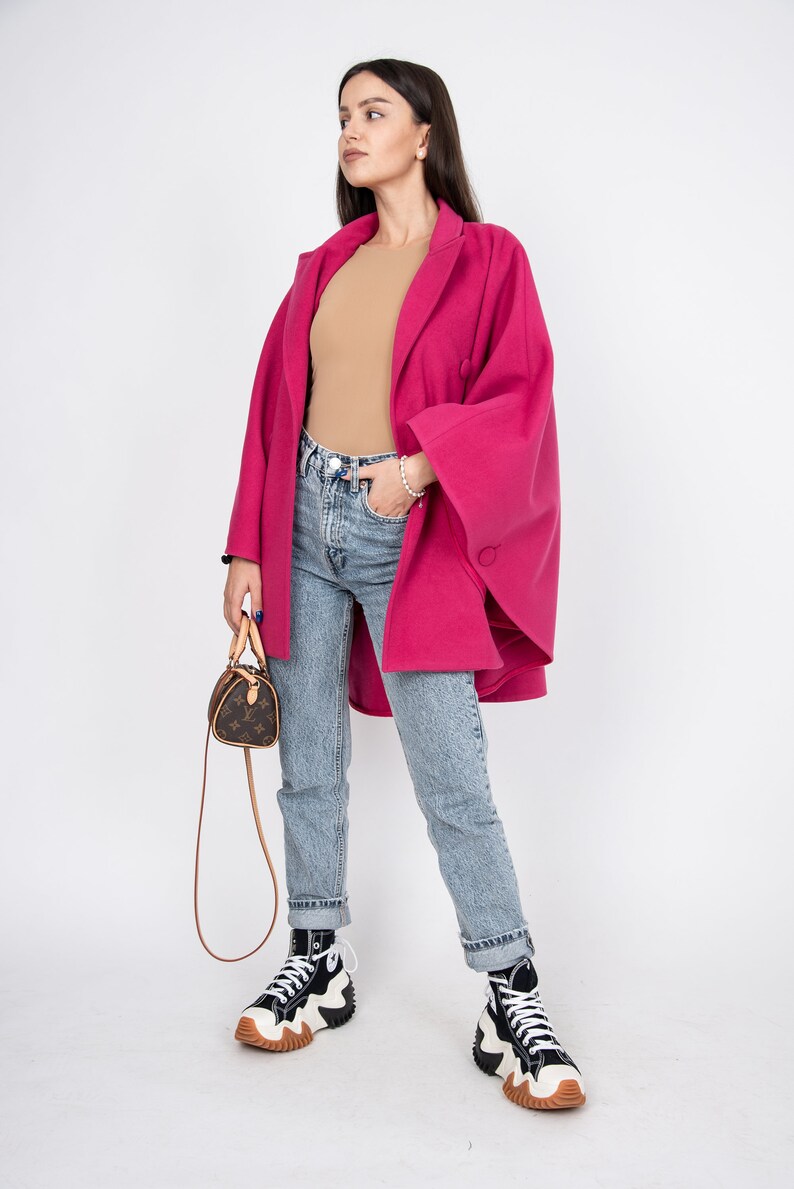 May include: A woman wearing a pink coat, blue jeans, and black and white high-top sneakers. She is carrying a small brown handbag with a strap.