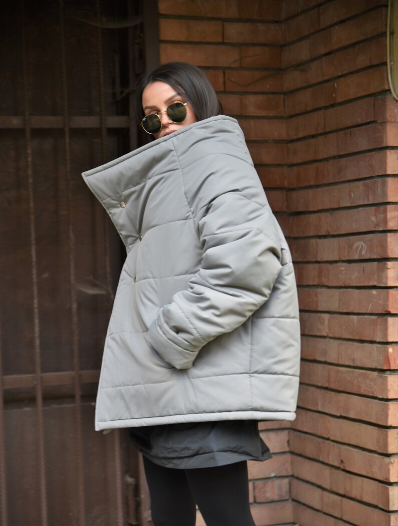 Peut inclure: Une veste matelass&eacute;e grise avec un col montant et une fermeture &eacute;clair. La veste a un design matelass&eacute; et une coupe ample.