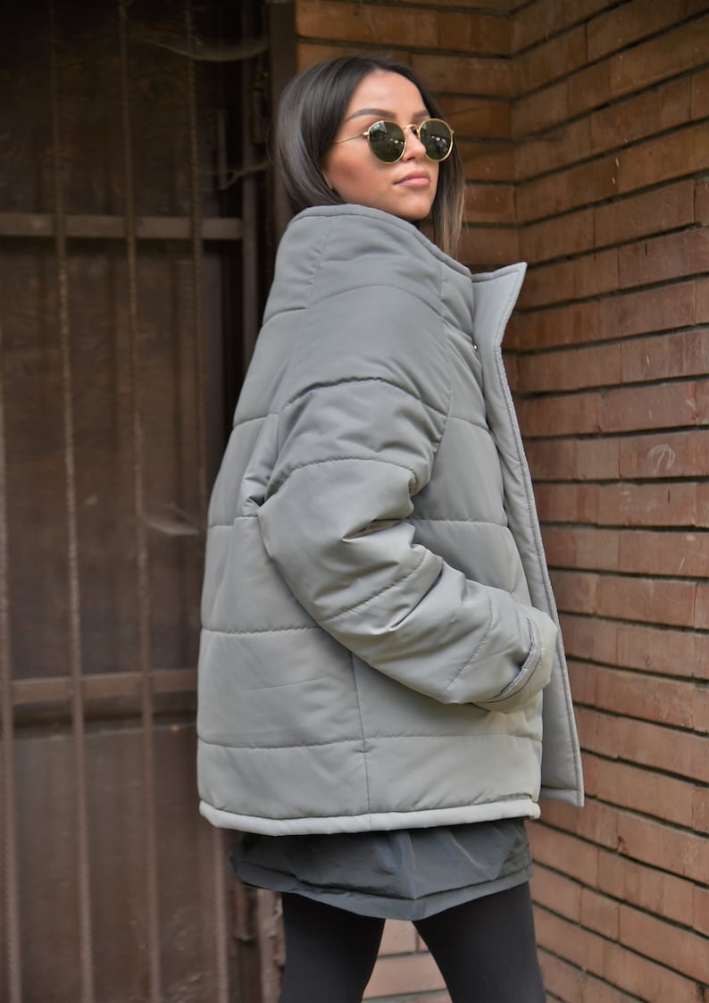 Peut inclure: Une veste matelass&eacute;e grise avec une fermeture &eacute;clair et un col montant. La veste a une coupe d&eacute;contract&eacute;e et est faite d'un mat&eacute;riau l&eacute;ger.