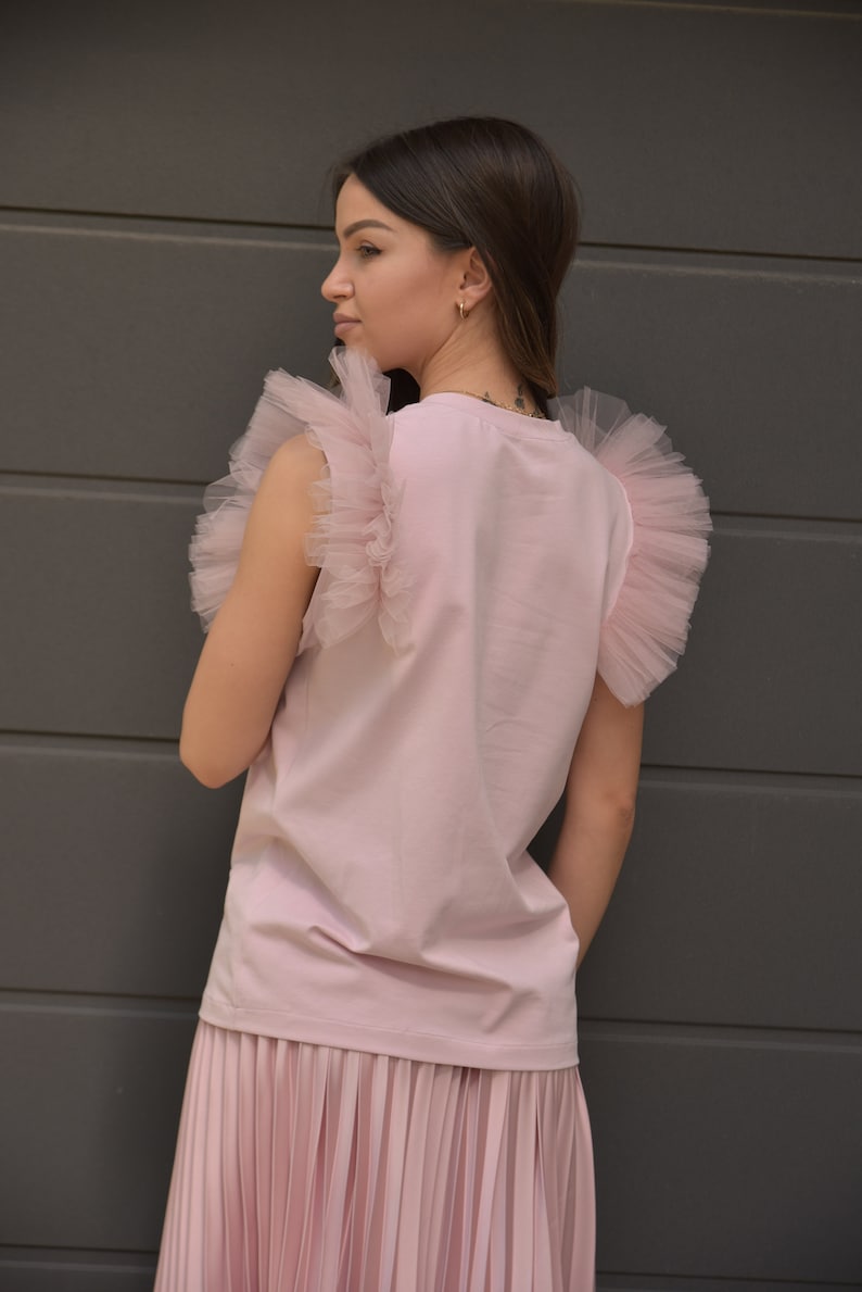 May include: A pink sleeveless top with tulle ruffles on the shoulders and a matching pleated skirt.